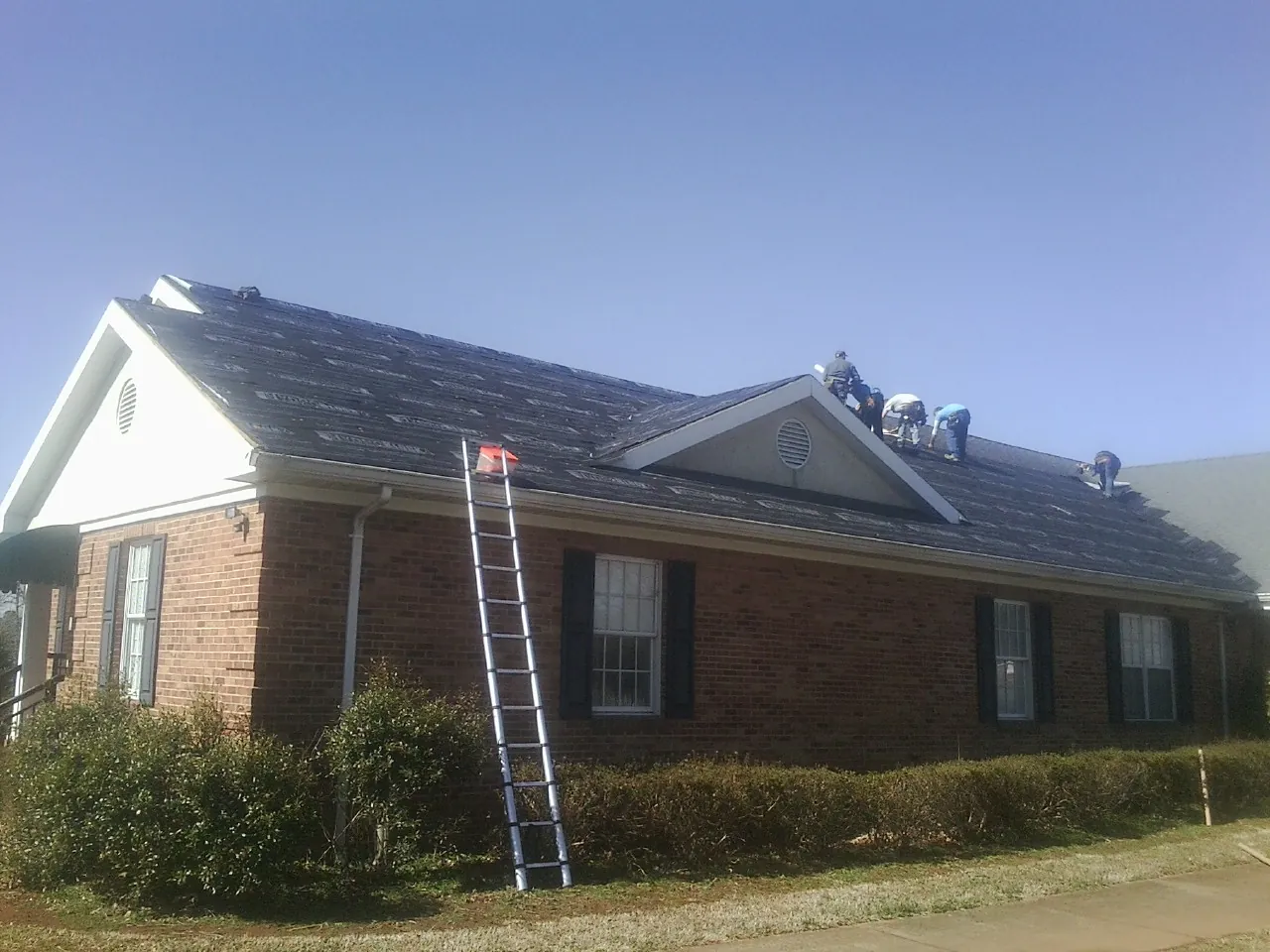 Crew tearing shingles off a brick ranch roof with a ladder set — Metal Roof Repair work by our crew in Cicero