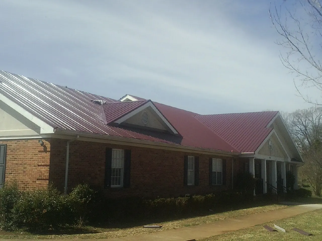 Red metal roof with gabled entries on a long brick building, from a Hail Damage Roof Repair job in Cicero